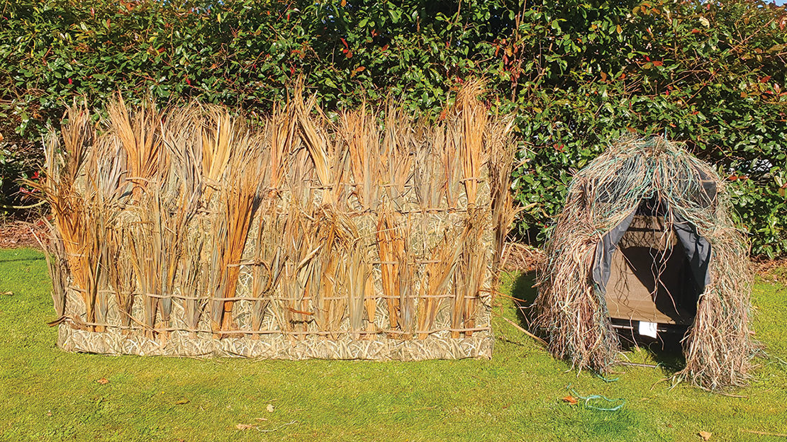 The A-frame is clad with dry cabbage tree fronds; the chair blind is covered in dyed raffia.
